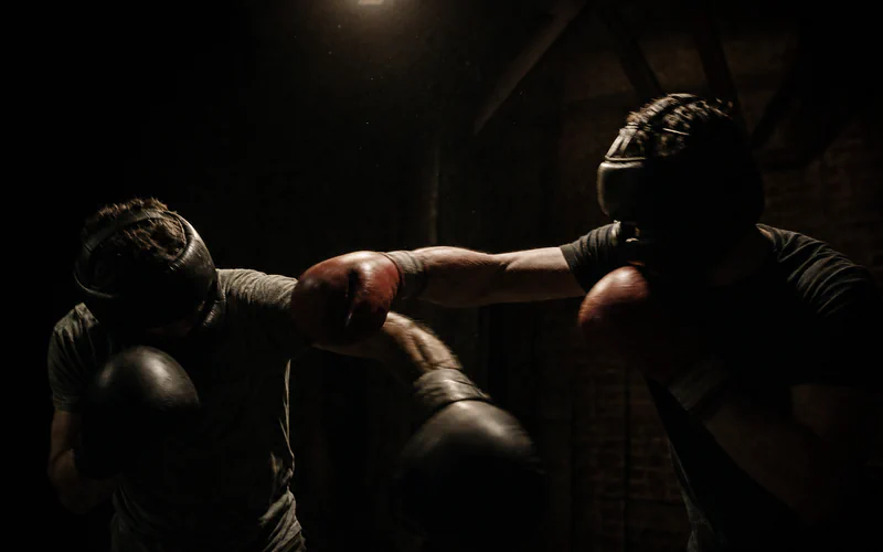 Dos personas haciendo sparring con cabezal y guantes, bajo una ampolleta